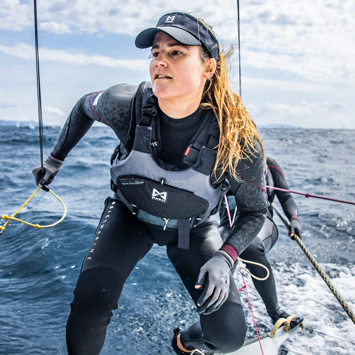 Woman on a sailboat in the ocean wearing a wetsuit and cap.