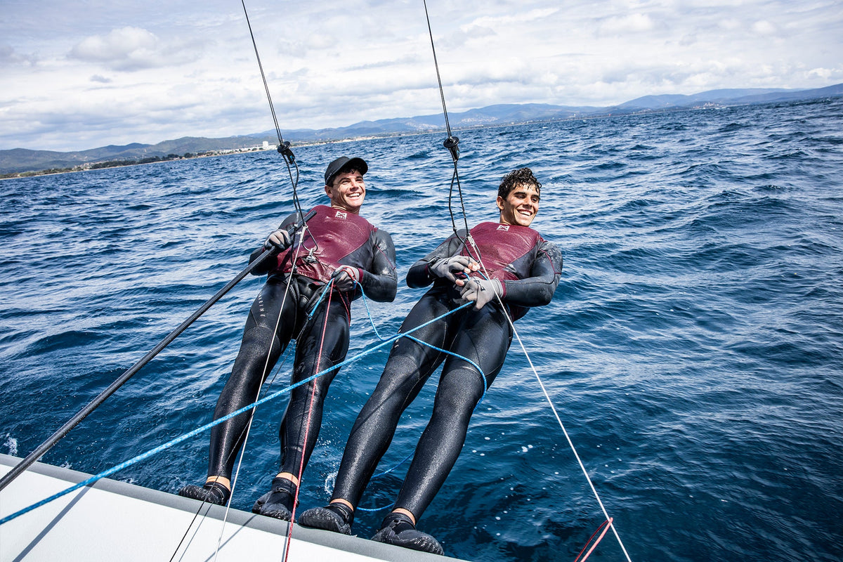 Two people in wetsuits on a sailboat in the ocean with a cloudy sky.